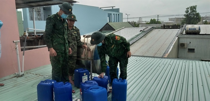 Cán bộ, chiến sĩ Đồn Biên phòng Non Nước giúp người dân trên địa bàn dùng can đựng nước chèn mái, hạn chế bị bay tôn khi gió to Ảnh: Trúc Hà