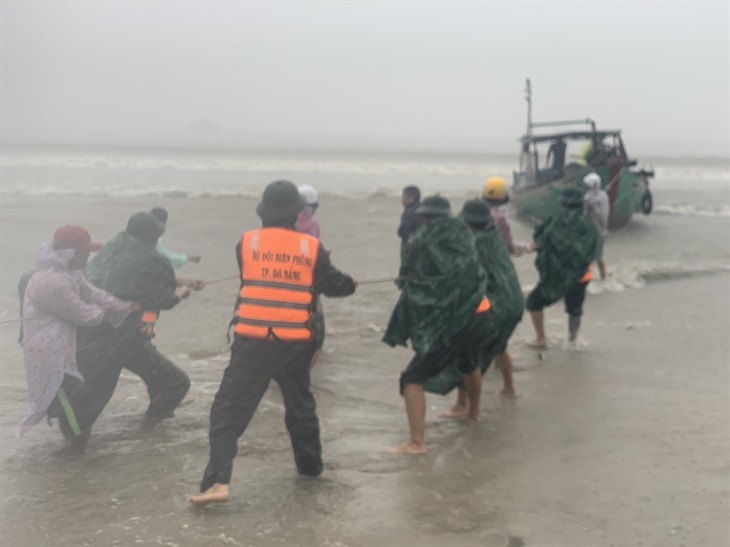 Cán bộ, chiến sĩ Đồn Biên phòng Hải Vân giúp ngư dân kéo tàu bị trôi dạt khi mưa to, sóng lớn. Ảnh: Trúc Hà